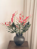 Red faux renanthera orchid arrangement with green leaves by FAUX Dubai