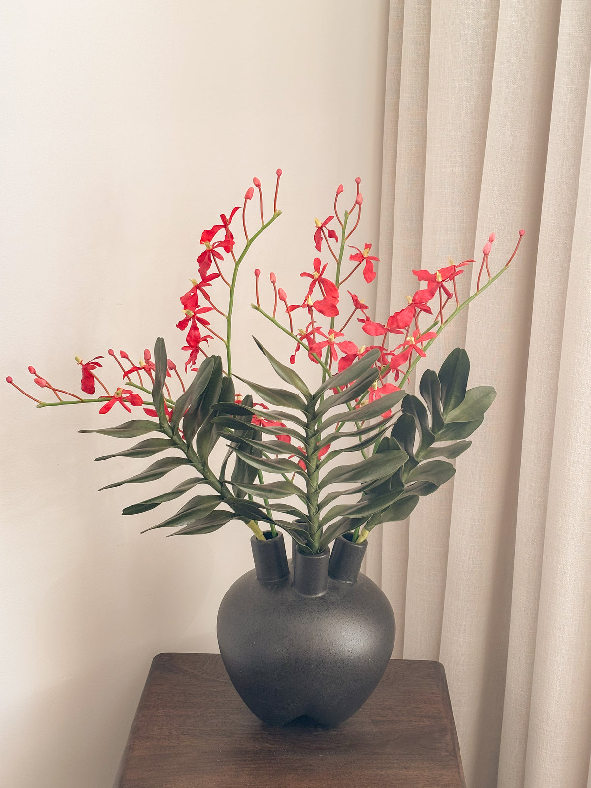 Red faux renanthera orchid arrangement with green leaves by FAUX Dubai